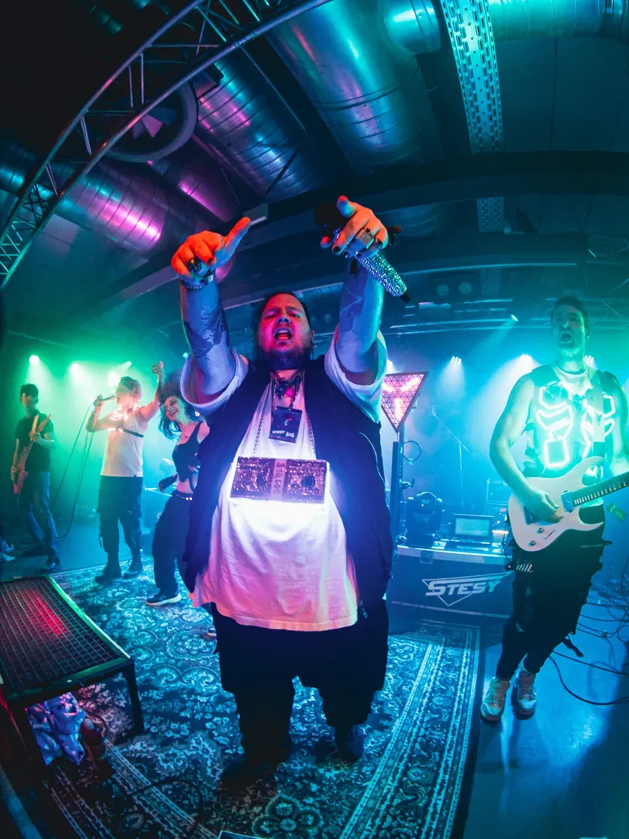 Saenger zeigt Teufelshoerner-Geste im gruenen Buehnenlicht