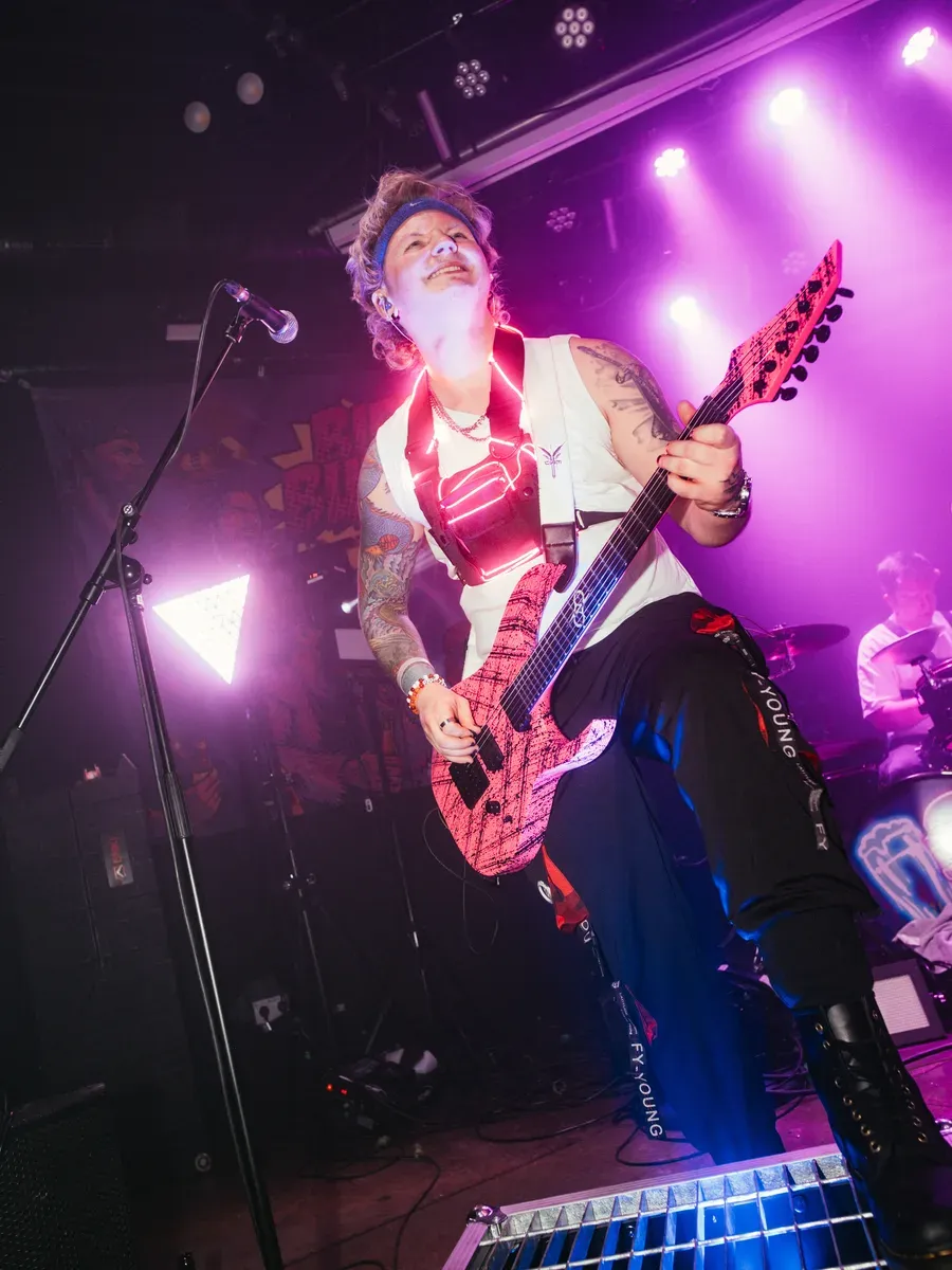 Bassist von unten mit pinker Gitarre und lila Buehnenlicht