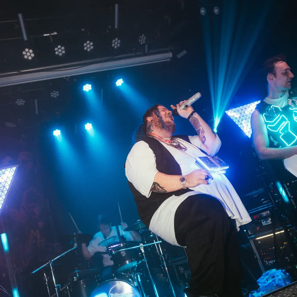 Saenger singt auf der Buehnenkante sitzend ins blaue Licht