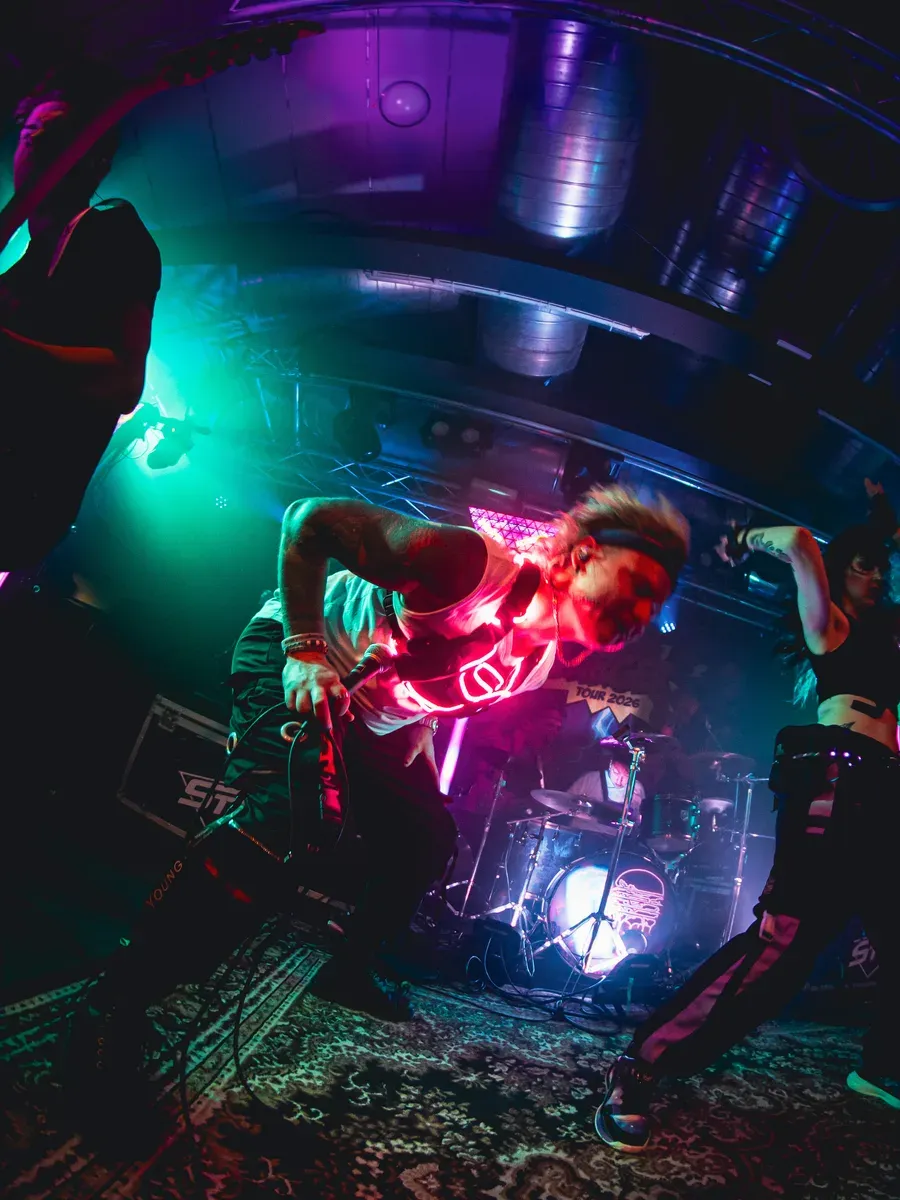 Bassist lehnt sich dynamisch zurueck unter gruen-lila Lichtern