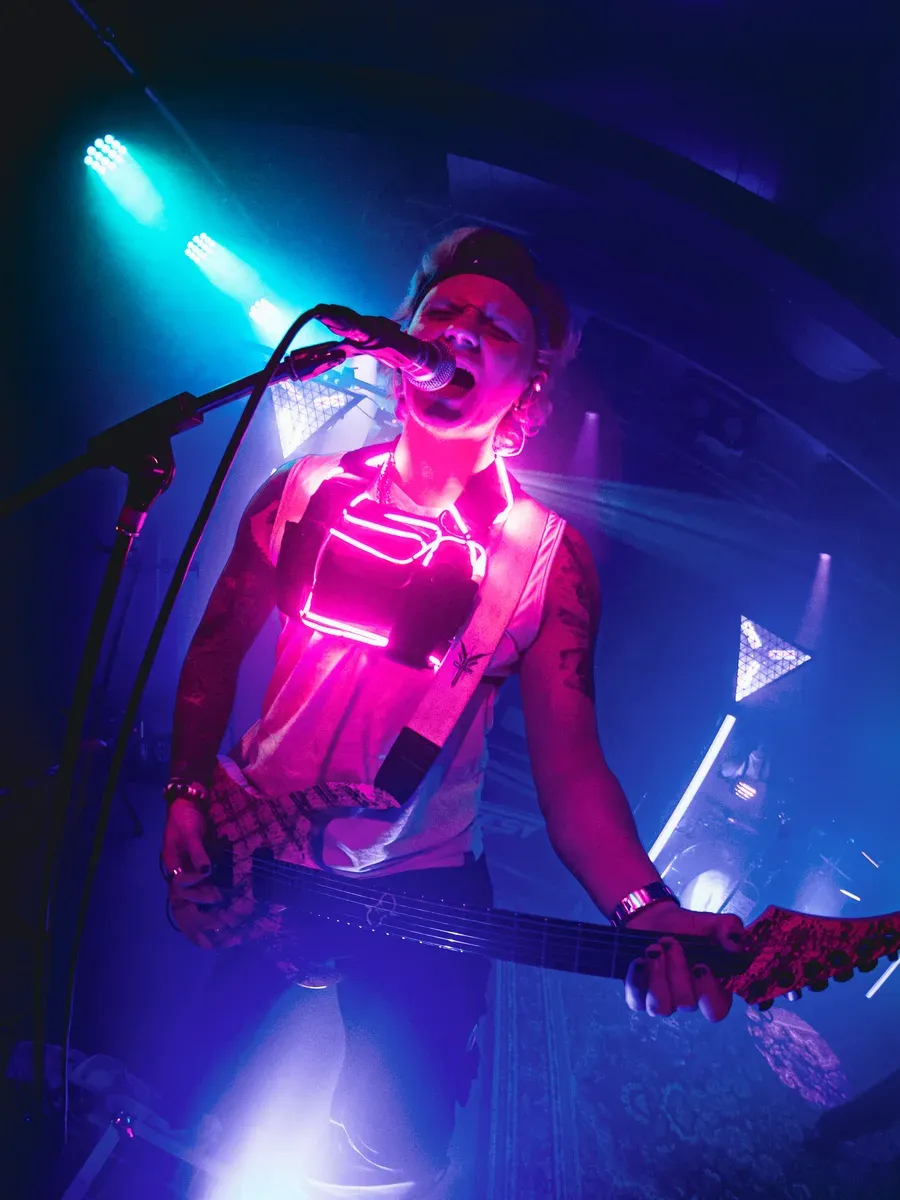 Bassist singt mit voller Kraft ins Mikrofon unter pinkem Neonlicht