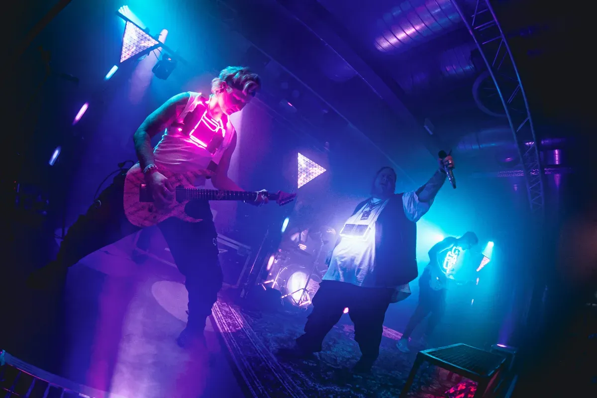 Bassist, Saenger und Gitarrist zusammen auf der Buehne im blau-lila Licht