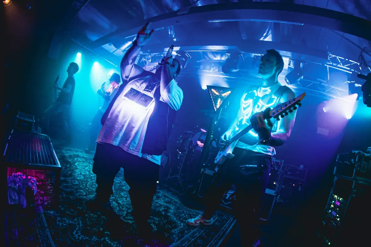 Saenger und Gitarrist von unten im blauen Buehnenlicht